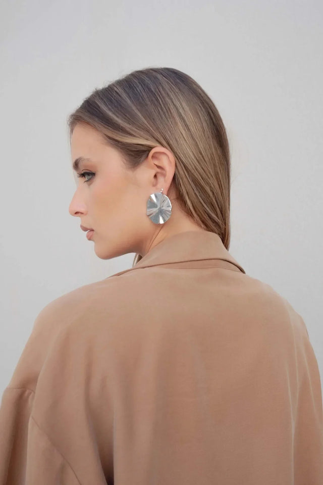 Vue de profil d'une femme en blazer fluide camel avec des boucles d'oreilles modernes.