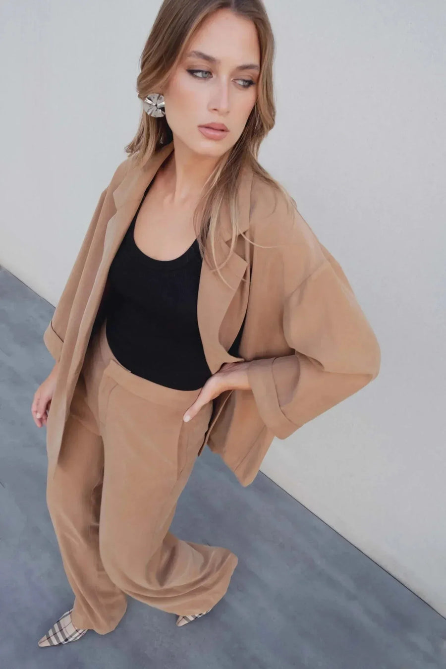 Vue plongeante de la femme en tailleur blazer fluide camel, complété par un haut noir et un pantalon ample.
