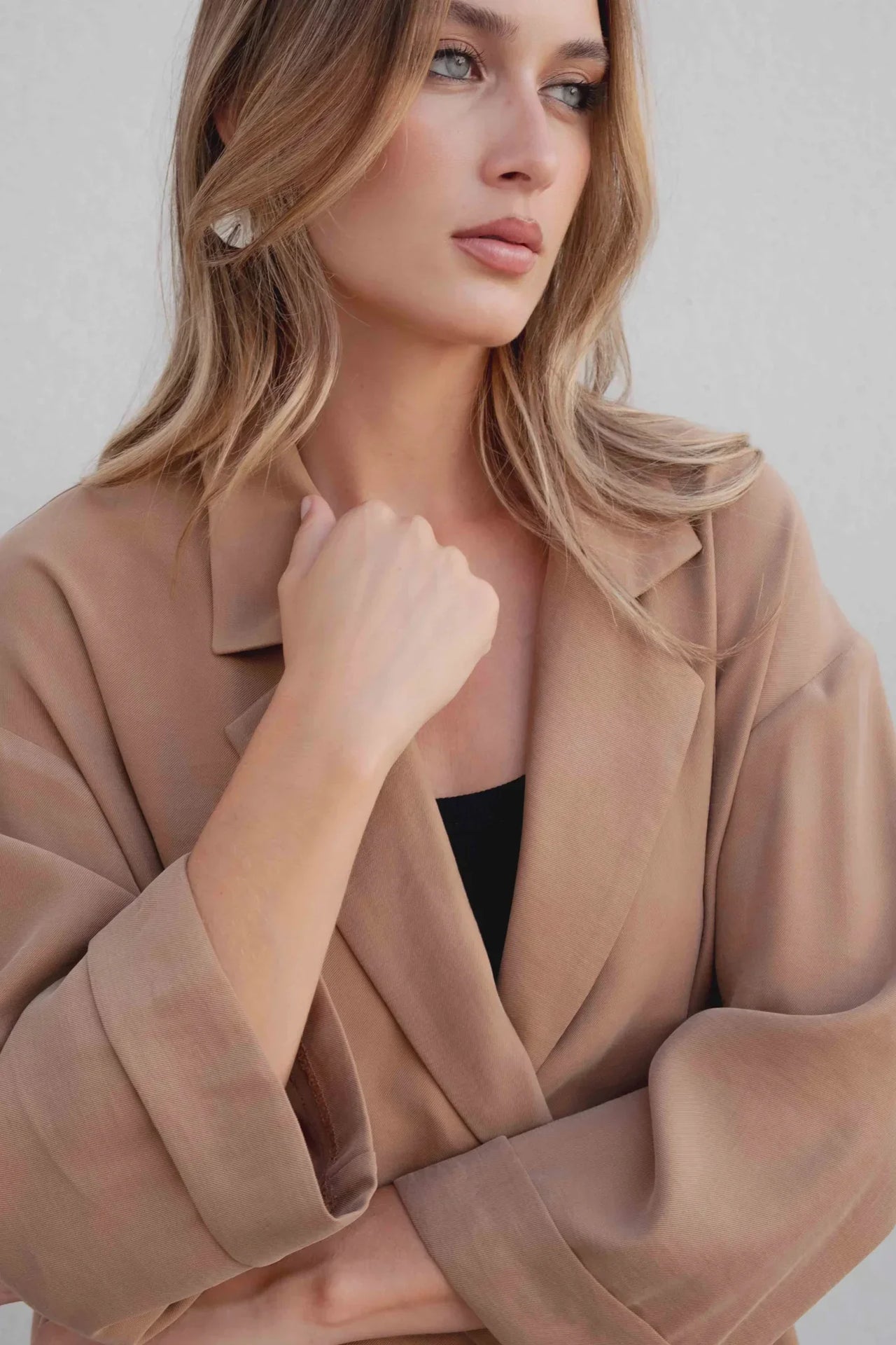Femme en tailleur blazer fluide camel, montrant une pose stylée avec les bras croisés.