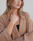 Femme en tailleur blazer fluide camel, montrant une pose stylée avec les bras croisés.