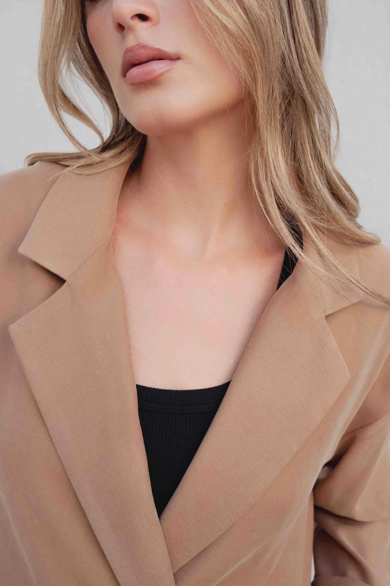 Zoom sur le col et le tissu d'un blazer fluide camel porté par une femme.