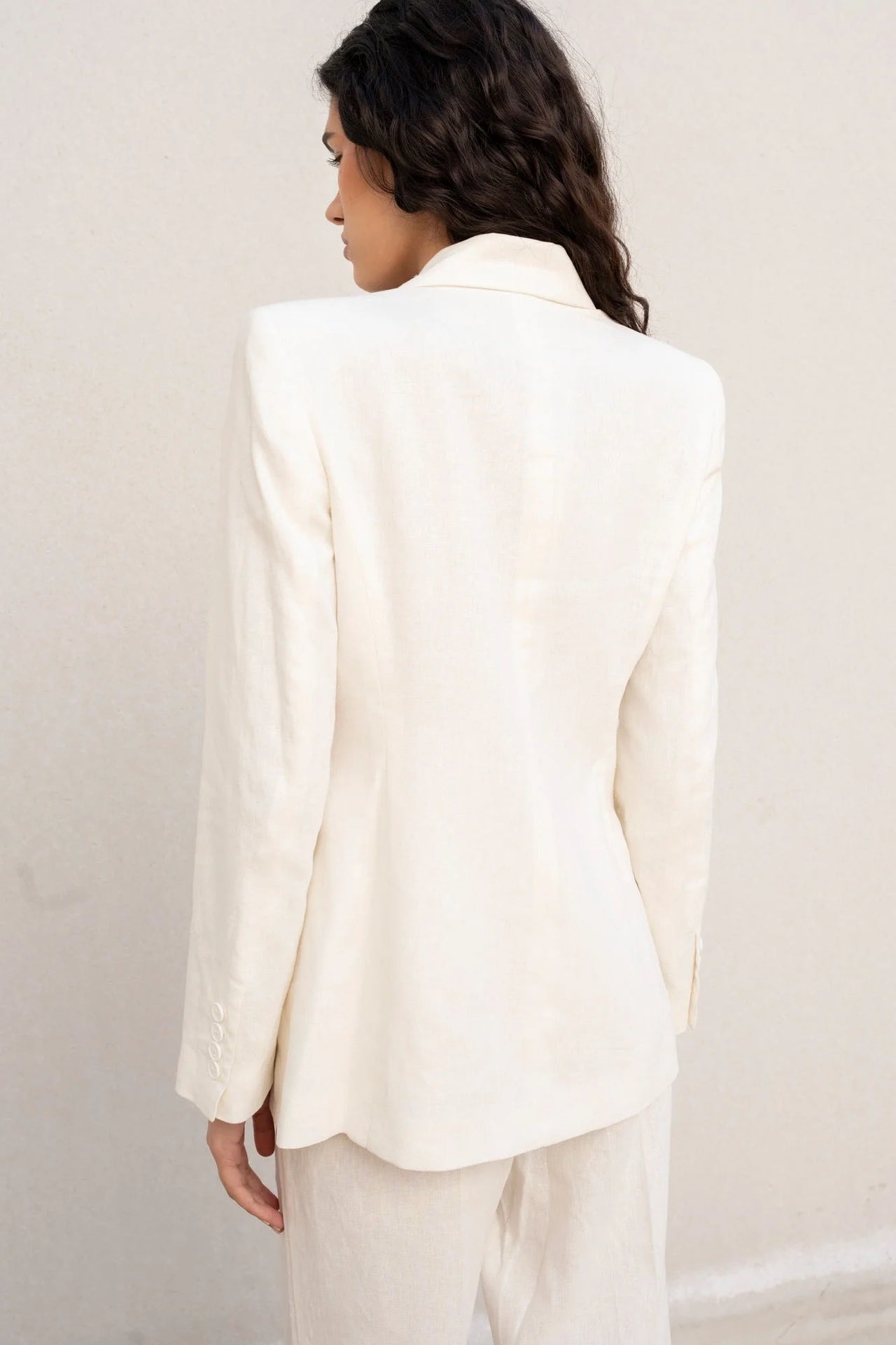 Vue arrière d'une femme portant un blazer blanc femme en lin naturel, soulignant la coupe structurée.