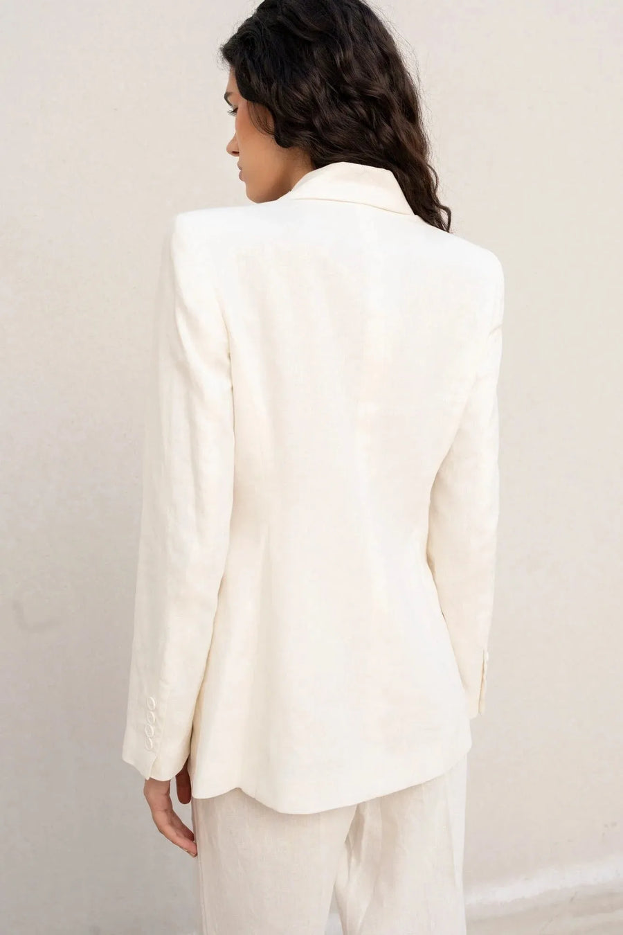 Vue arrière d'une femme portant un blazer blanc femme en lin naturel, soulignant la coupe structurée.