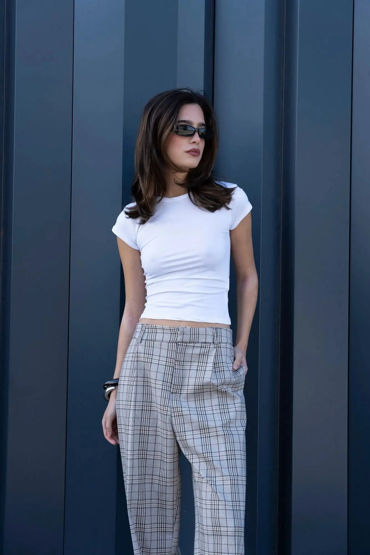 Modèle posant en extérieur avec un tee-shirt blanc et un tailleur pantalon à carreaux beige look structuré, affichant un look moderne et élégant. Pantalon femme carreaux.
