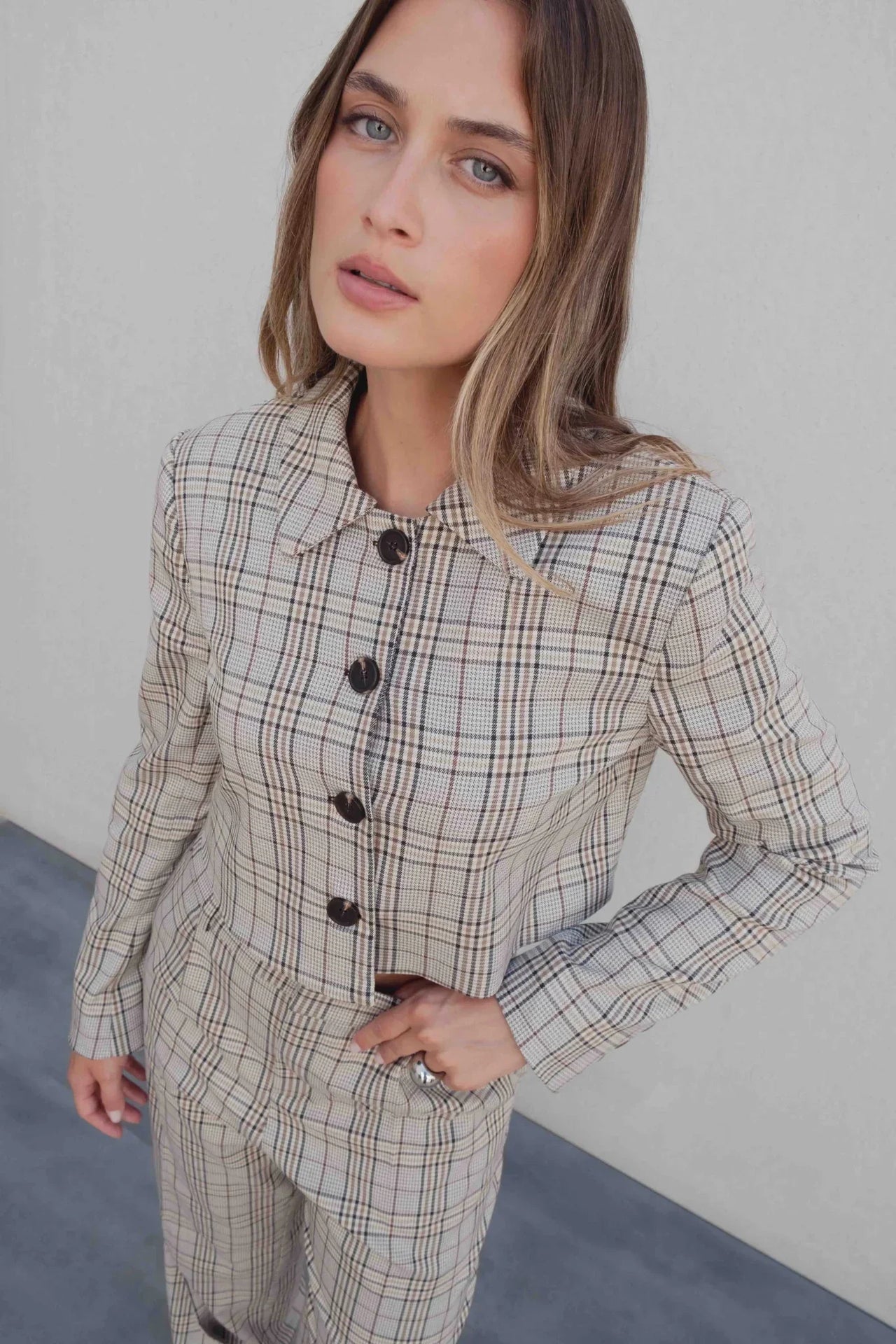 Femme portant un tailleur pantalon à carreaux beige look structuré, style chic avec un col et des boutons sur l'ensemble du haut, parfait pour un look élégant. Pantalon femme carreaux.
