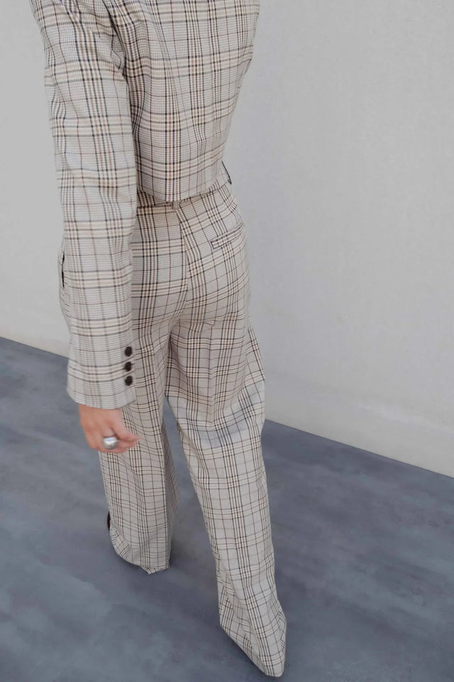 Vue arrière d'une femme en tailleur pantalon à carreaux beige look structuré, montrant la silhouette stylée et la coupe fluide, idéale pour un style chic. Pantalon femme carreaux.