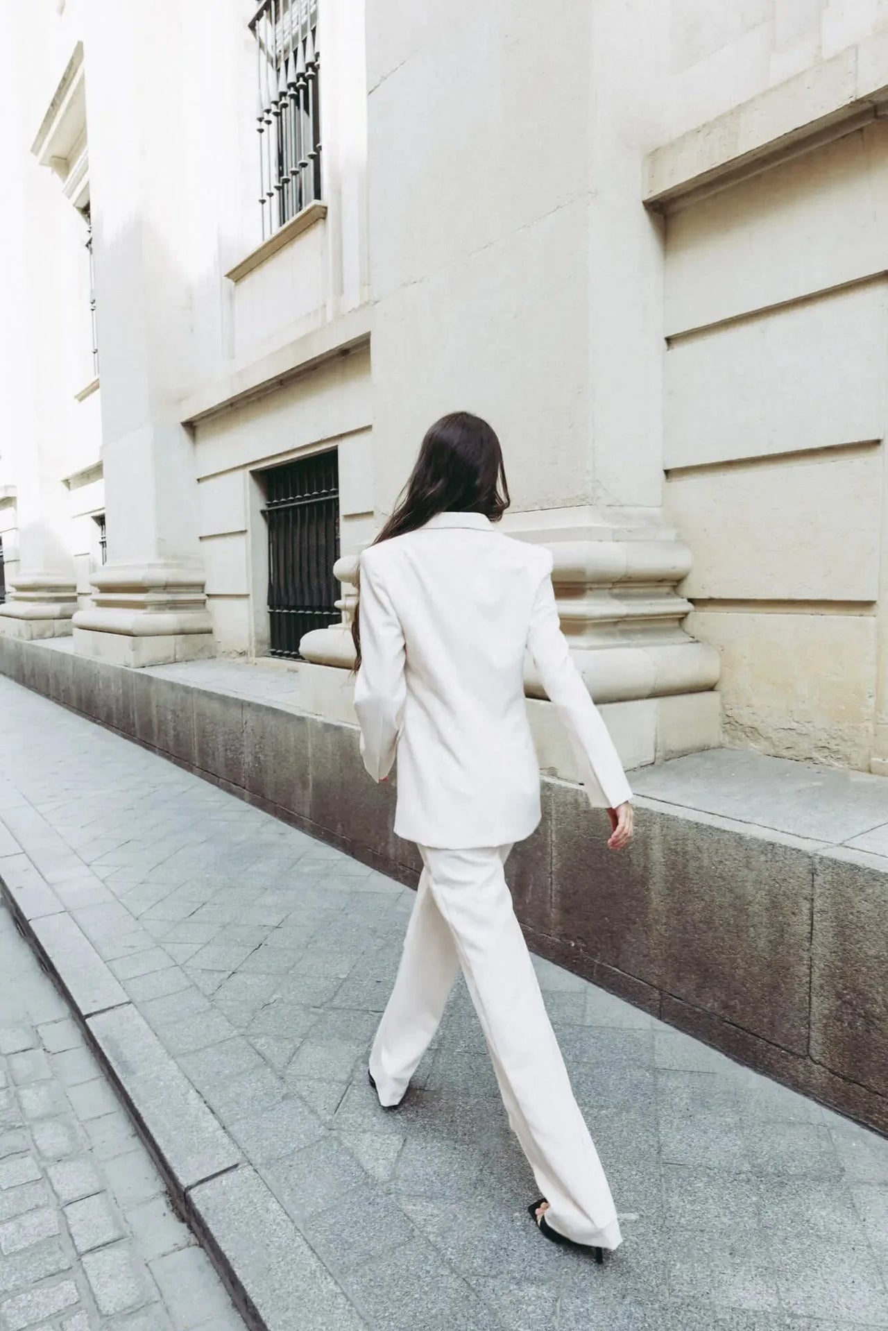Vue de dos d'une femme en tailleur pantalon ample crème, démontrant la coupe élégante du pantalon pince femme.