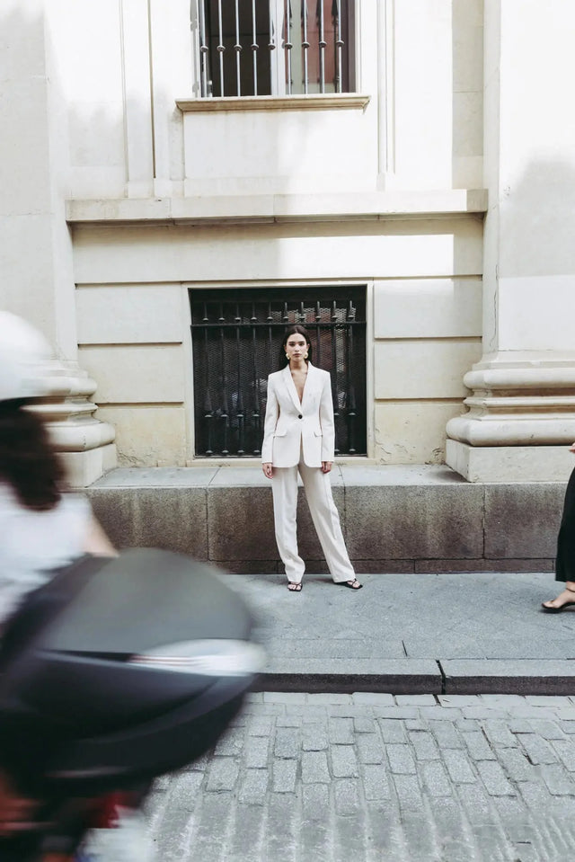 Femme en tailleur pantalon ample crème se tenant droite, arborant un style chic, parfait pour un pantalon pince femme.