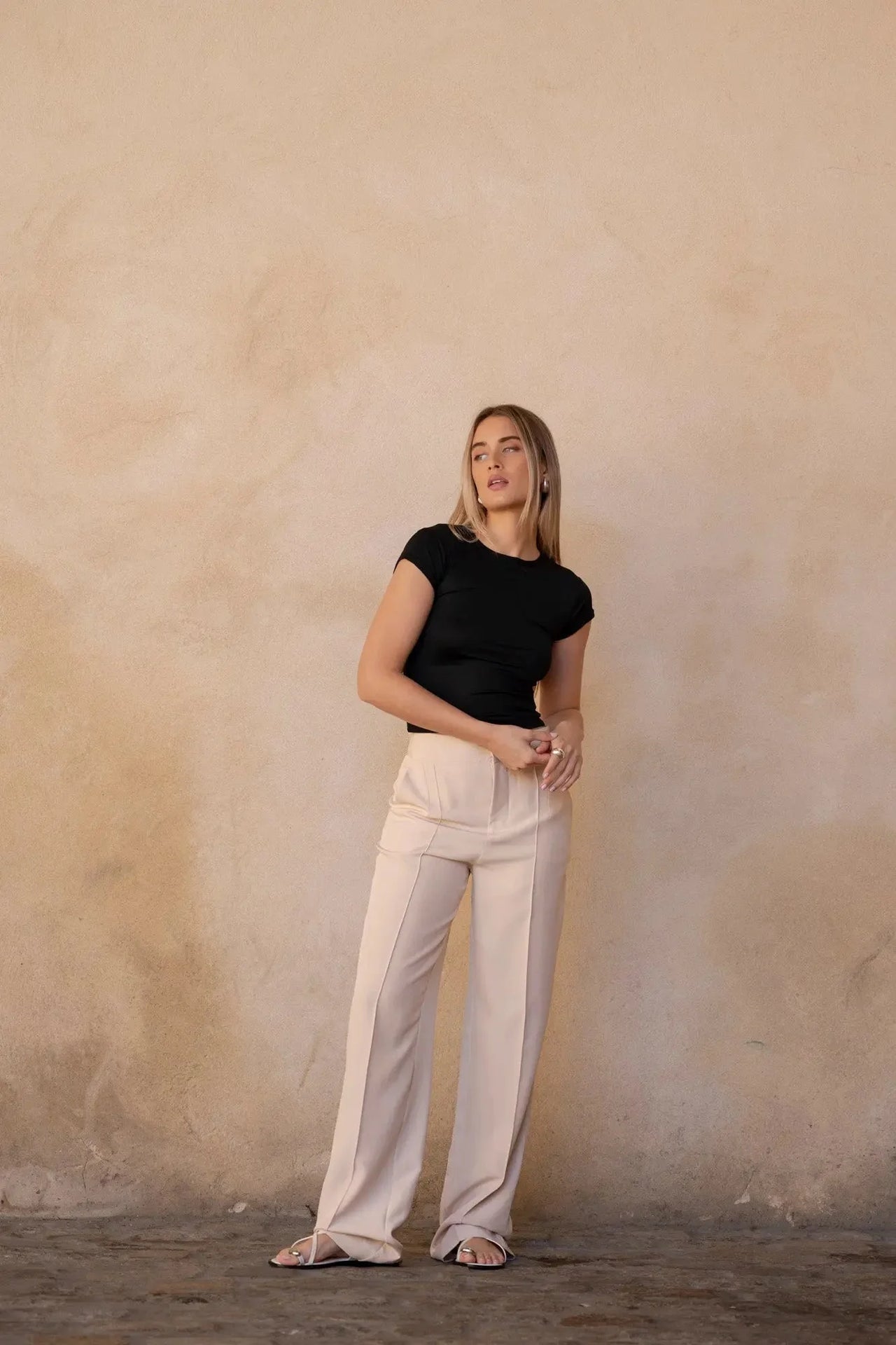 Femme posant contre un mur dans un look décontracté associé à un pantalon ample crème, mettant en lumière le pantalon pince femme.