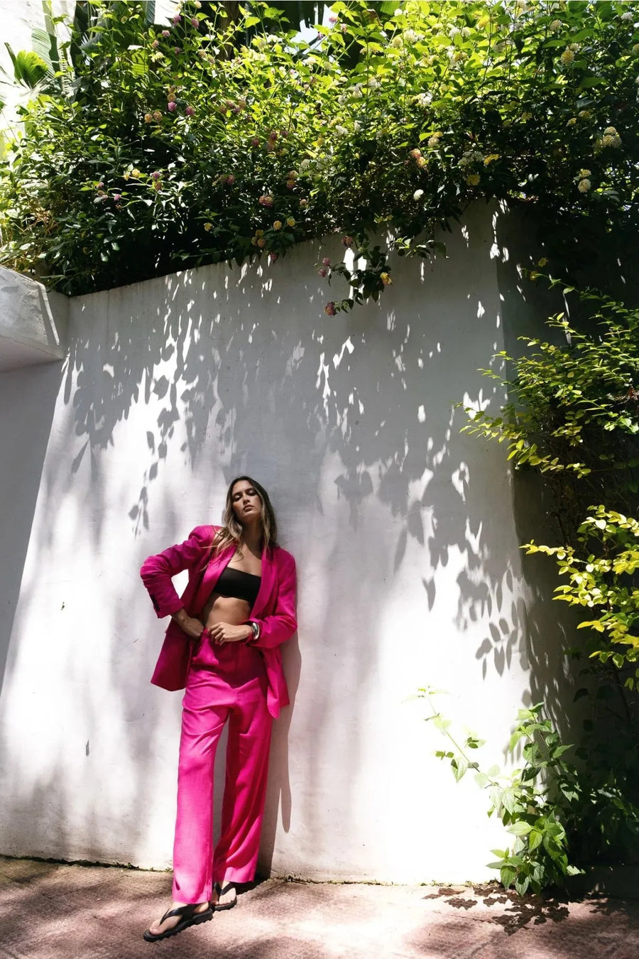 Femme en tailleur pantalon en lin rose fuchsia devant un mur, blazer rose fuchsia femme, style chic.