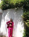 Femme en tailleur pantalon en lin rose fuchsia devant un mur, blazer rose fuchsia femme, style chic.