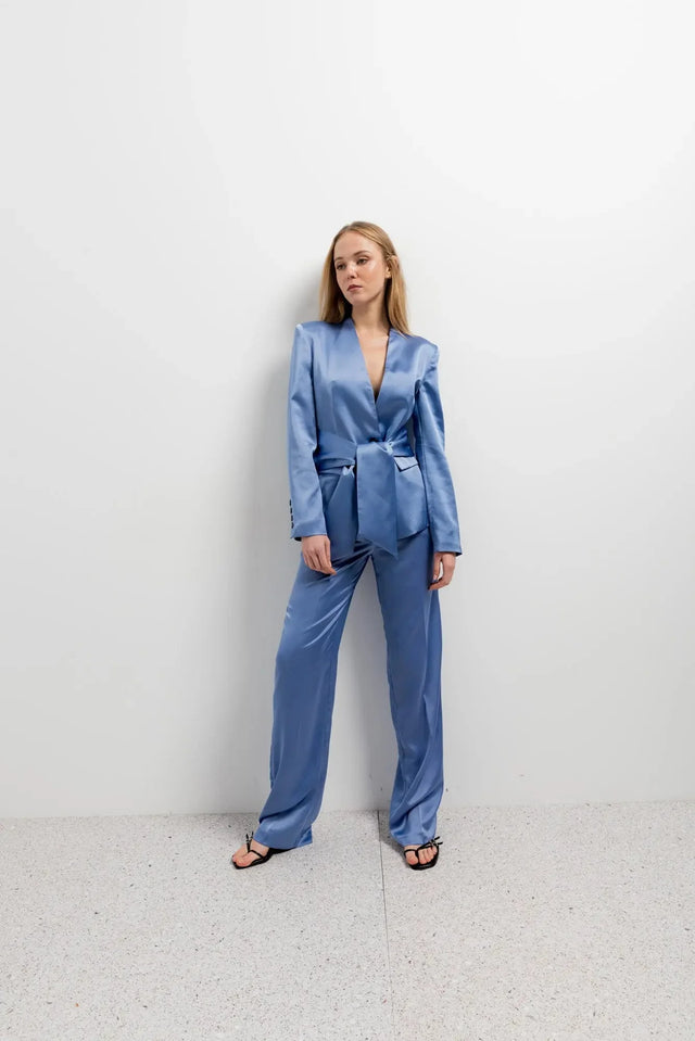 Modèle portant un tailleur pantalon en satin bleu ceinturé, parfait pour une allure chic. Idéal pour une femme à la recherche d'un blazer satin femme élégant.