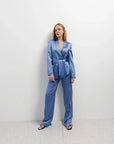 Modèle portant un tailleur pantalon en satin bleu ceinturé, parfait pour une allure chic. Idéal pour une femme à la recherche d'un blazer satin femme élégant.