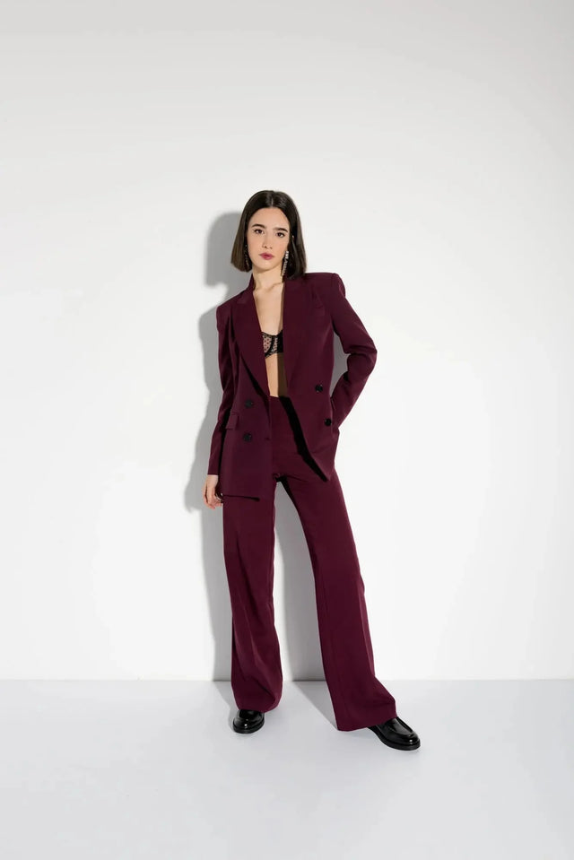 Femme posant avec style dans un blazer femme bordeaux double boutonnage croisé, complété par un pantalon assorti.