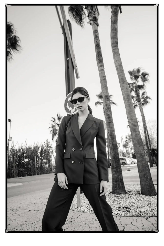 Portrait d'une femme en extérieur, arborant un blazer femme bordeaux double boutonnage croisé, lunettes de soleil, affichant une allure sophistiquée.