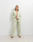 Femme en pantalon vert femme et blazer, saisissant l'attention avec son style moderne et tendance dans une ambiance lumineuse.