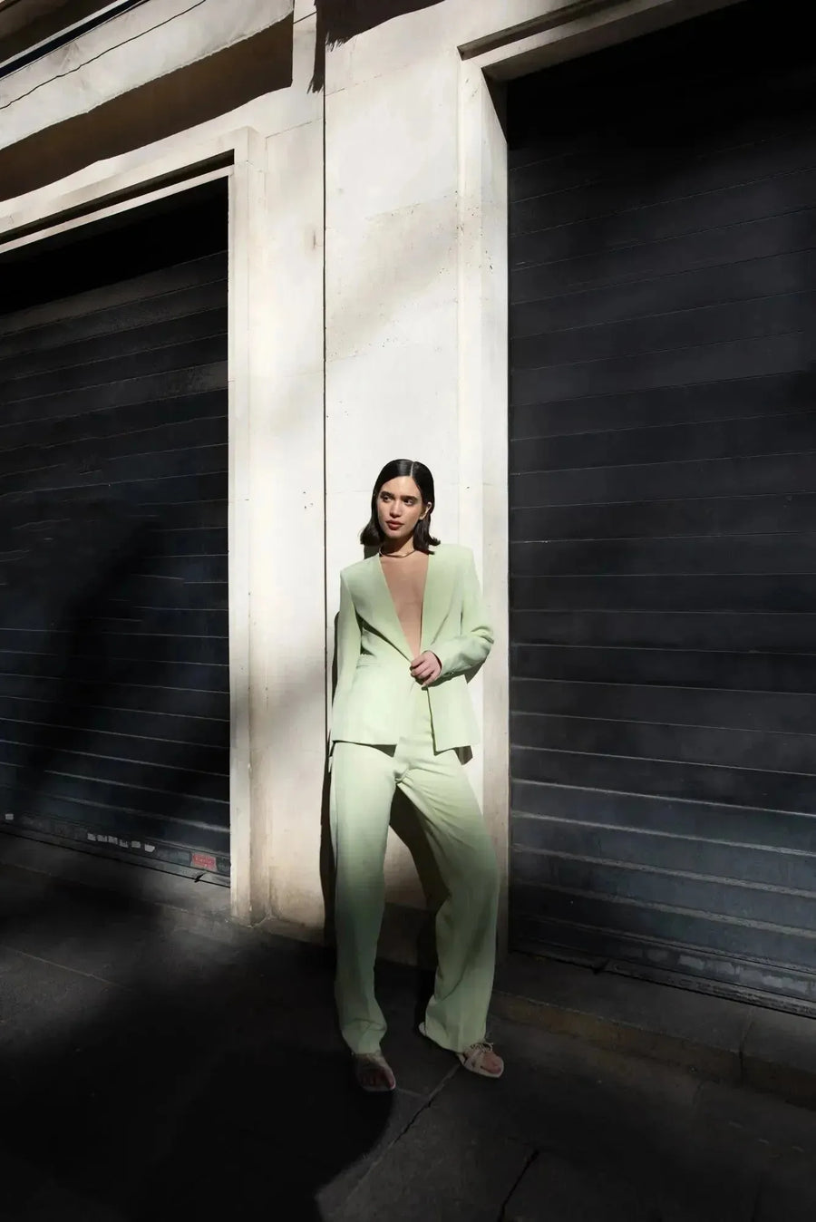 Femme portant un pantalon vert femme droit confortable et élégant de Sapiato, avec un blazer assorti, posant contre un mur moderne.