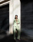 Femme portant un pantalon vert femme droit confortable et élégant de Sapiato, avec un blazer assorti, posant contre un mur moderne.