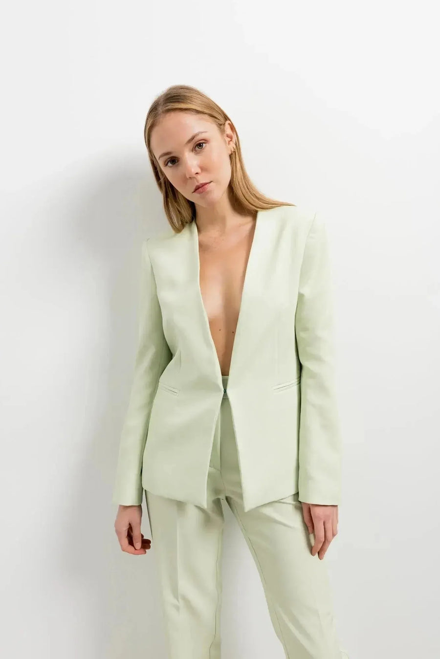 Modèle féminin affichant le pantalon vert femme dans un cadre minimaliste, avec un blazer décontracté et un look élégant.