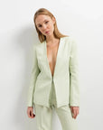 Modèle féminin affichant le pantalon vert femme dans un cadre minimaliste, avec un blazer décontracté et un look élégant.