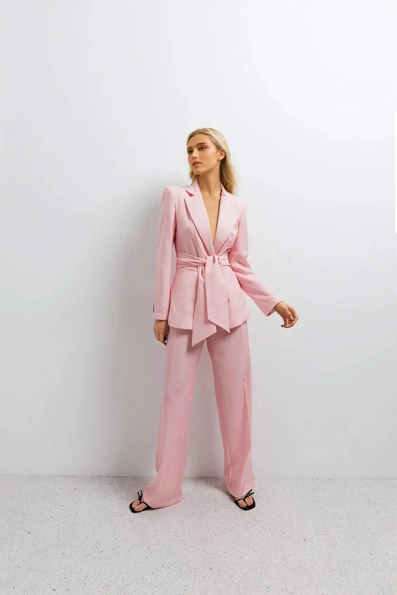 Pantalon rose femme ceinturé pour toutes occasions, modèle féminin en pose raffinée avec un blazer rose sur fond neutre.