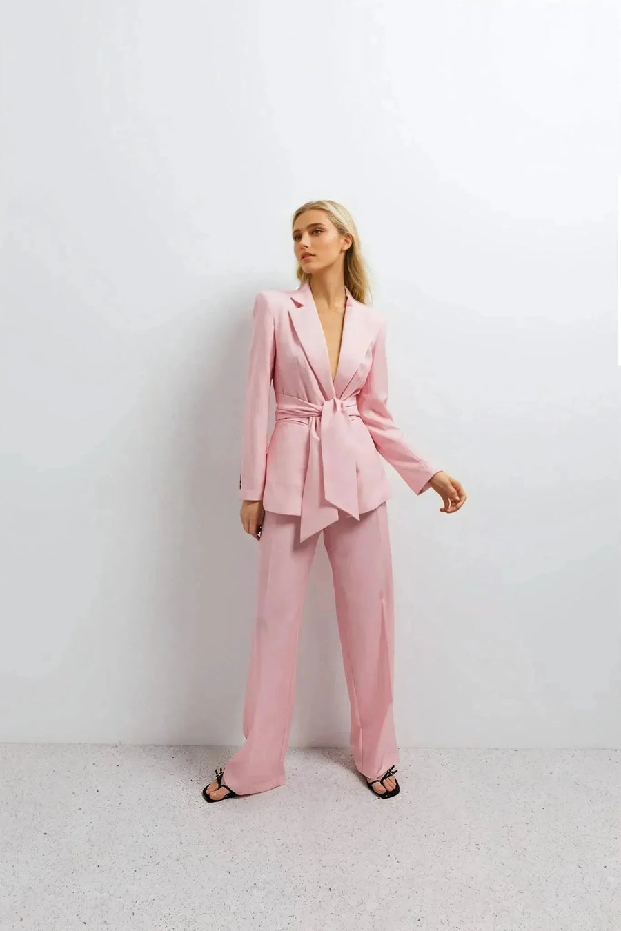 Pantalon rose femme ceinturé pour toutes occasions, modèle féminin en pose raffinée avec un blazer rose sur fond neutre.