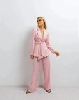 Pantalon rose femme ceinturé pour toutes occasions, modèle féminin en pose raffinée avec un blazer rose sur fond neutre.