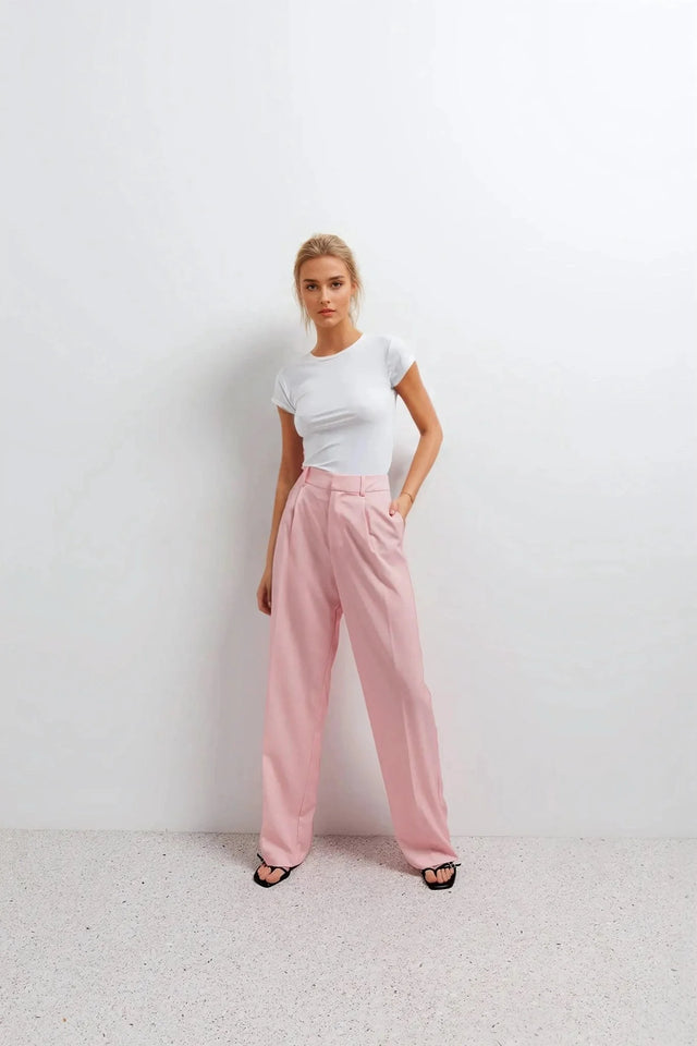 Pantalon rose femme ceinturé pour toutes occasions, femme stylée en tee-shirt blanc et pantalon rose, pose moderne et confiante.