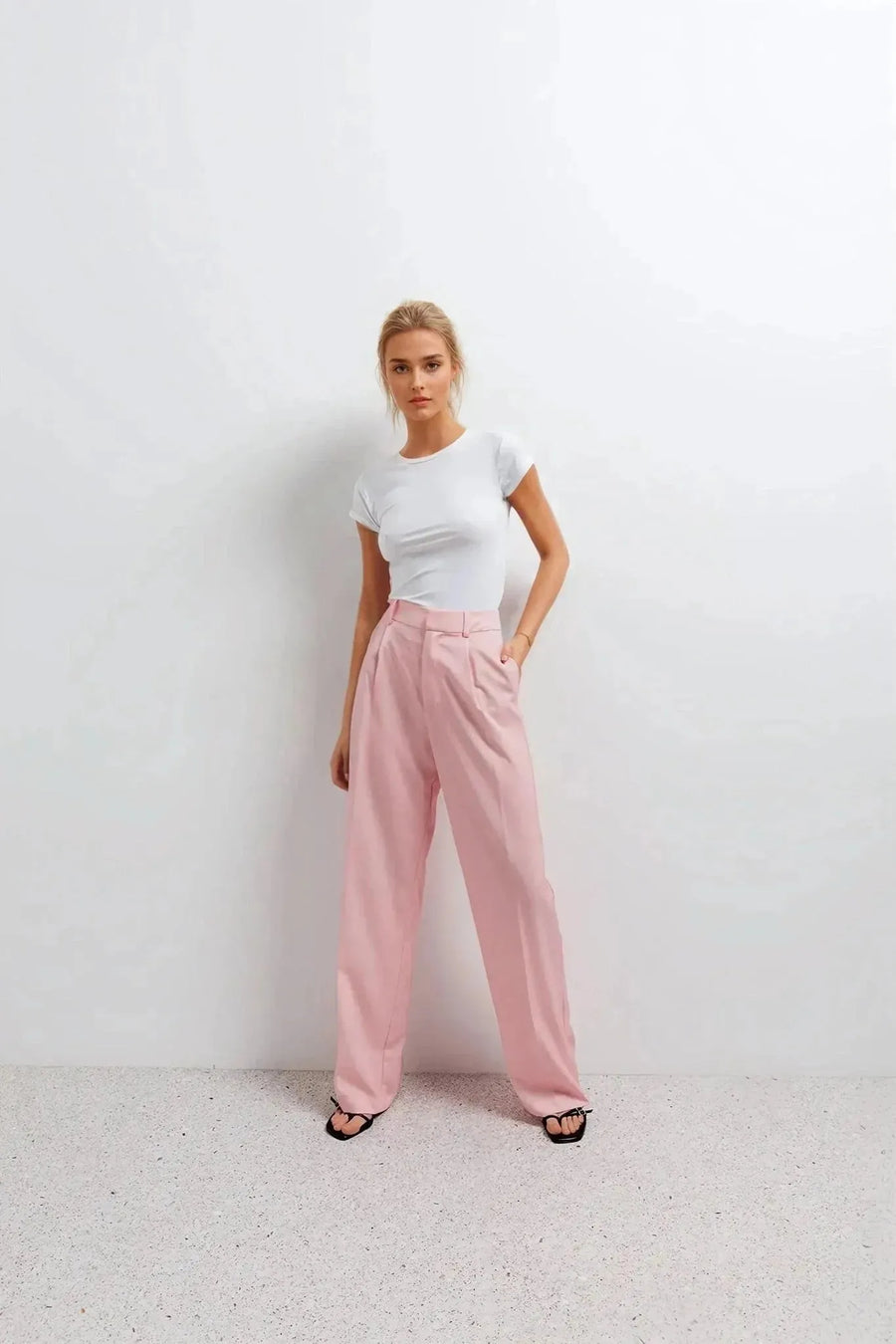 Pantalon rose femme ceinturé pour toutes occasions, femme stylée en tee-shirt blanc et pantalon rose, pose moderne et confiante.