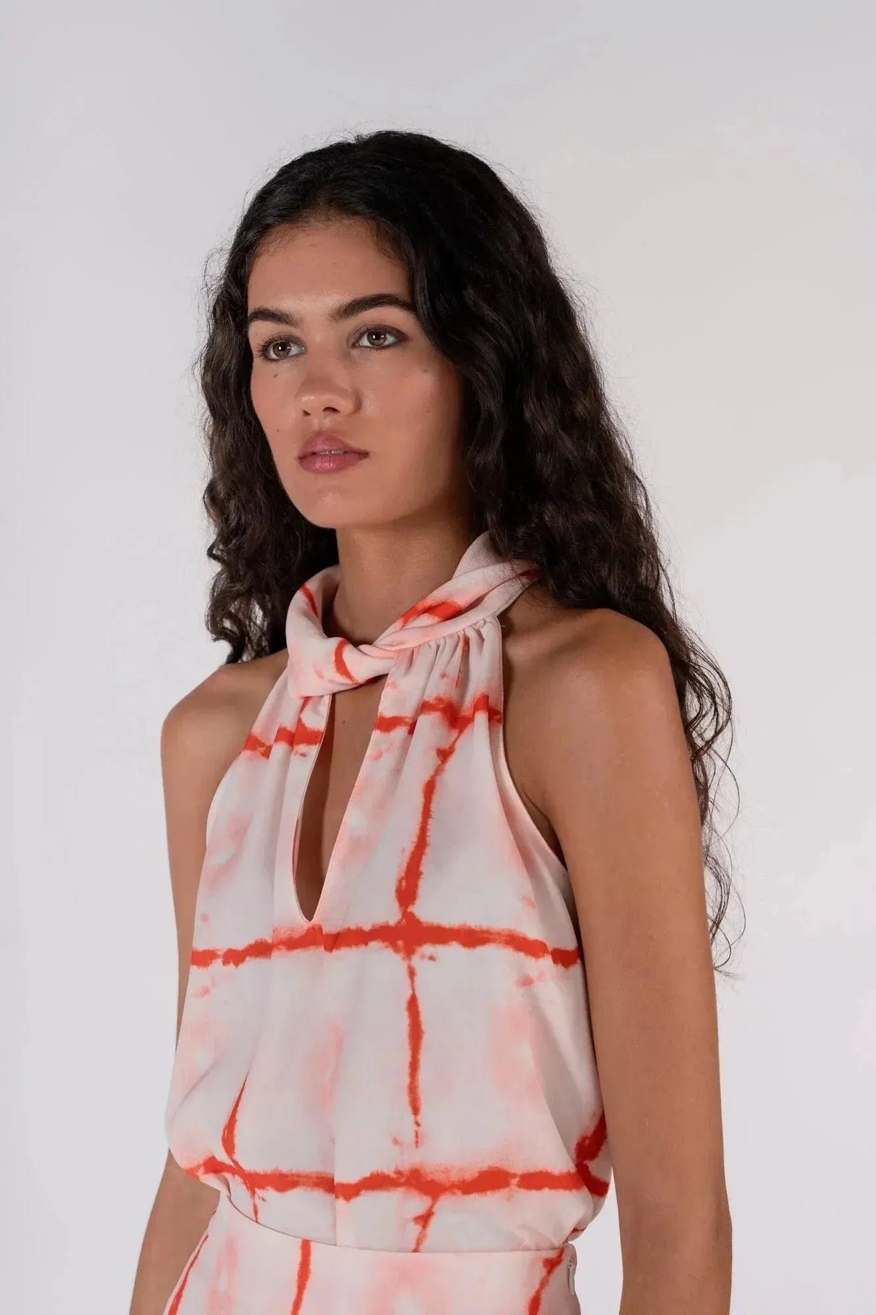 Gros plan sur le visage d'une femme avec le Top Col Halter Imprimé Graphique Rouge Et Blanc, soulignant le col ouvert et le style raffiné.