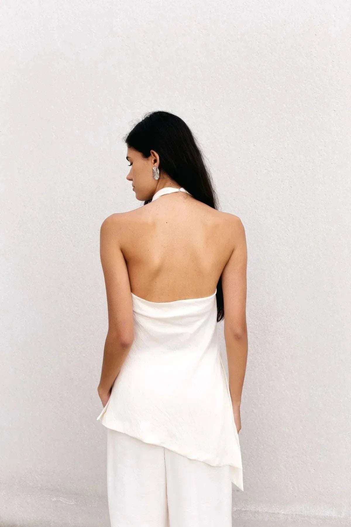 Vue arrière du haut dos nu femme chic Ivoire à col montant halter, mettant en avant le dos dénudé et la coupe asymétrique, mannequin avec des accessoires modernes.