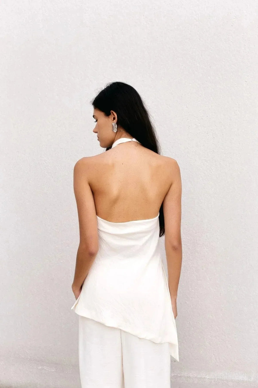 Vue arrière du haut dos nu femme chic Ivoire à col montant halter, mettant en avant le dos dénudé et la coupe asymétrique, mannequin avec des accessoires modernes.