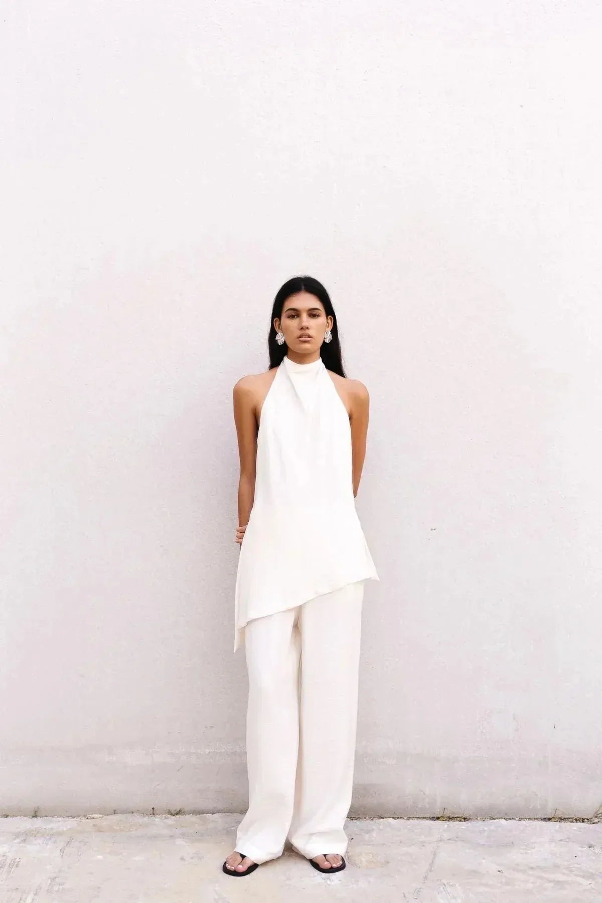 Mannequin portant le haut dos nu femme chic Ivoire à col montant halter avec un pantalon assorti, pose moderne sur fond épuré.