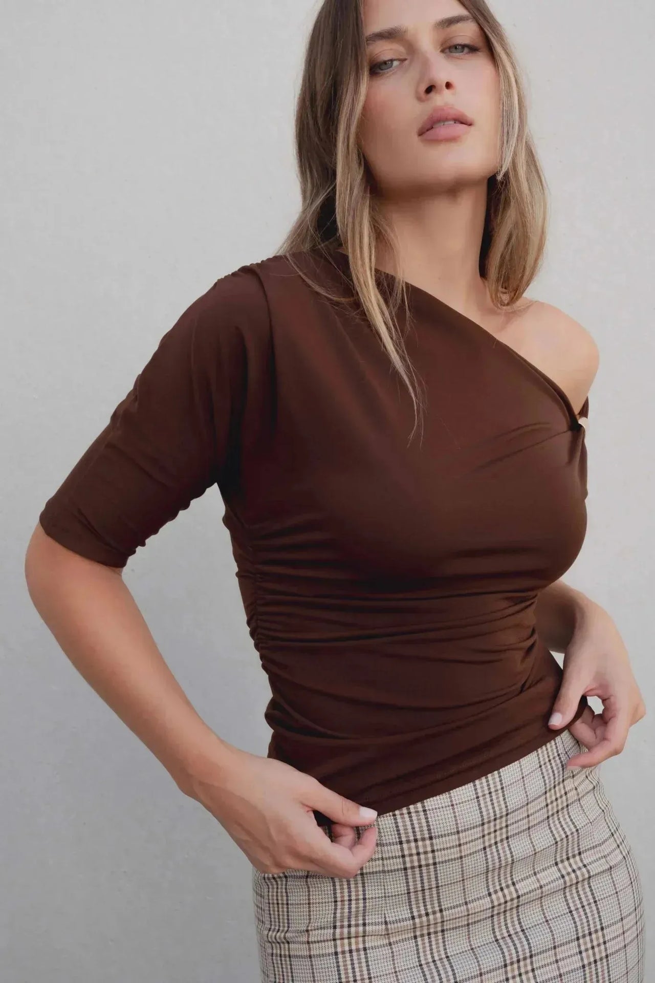 Gros plan sur un haut marron, accompagné d'une jupe midi femme à carreaux Prince De Galles, soulignant un look moderne et élégant.