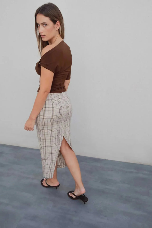 Femme en profil mettant en avant la fente arrière de sa jupe midi femme à carreaux Prince De Galles, avec un haut marron.