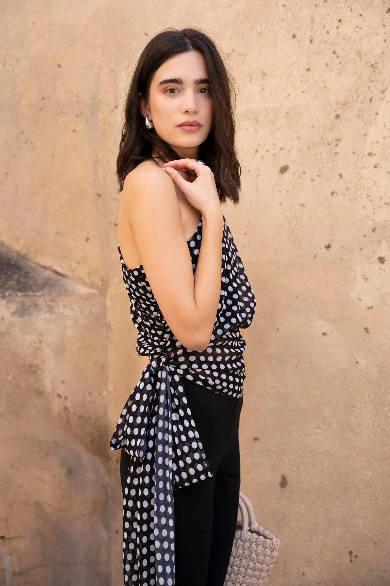 Femme portant un top asymétrique imprimé à pois noirs et blancs et un sac en osier
