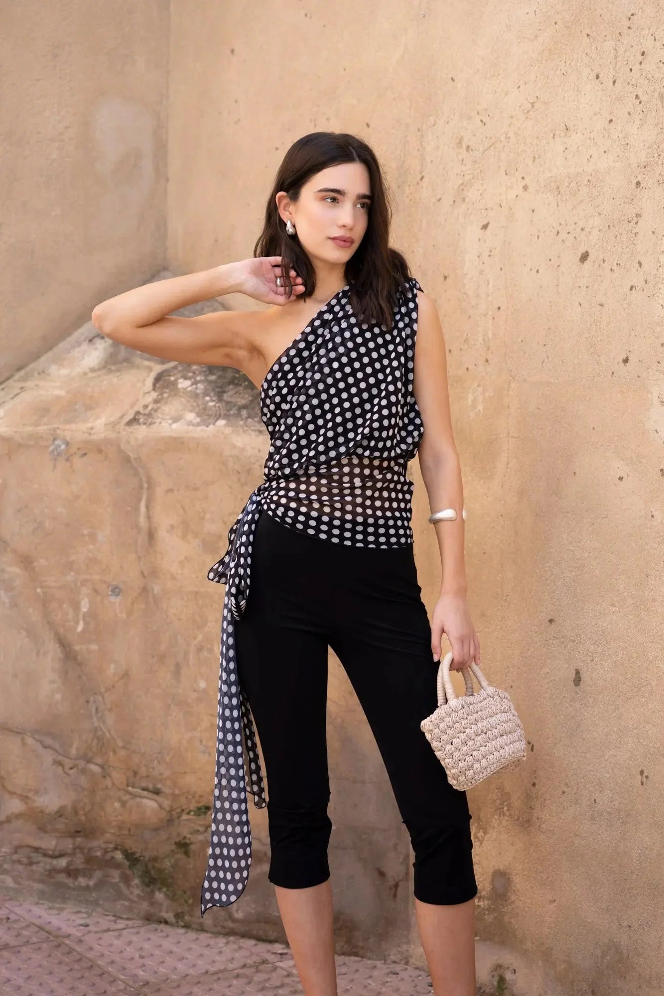 Femme portant un top asymétrique imprimé à pois noirs et blancs et un sac en osier