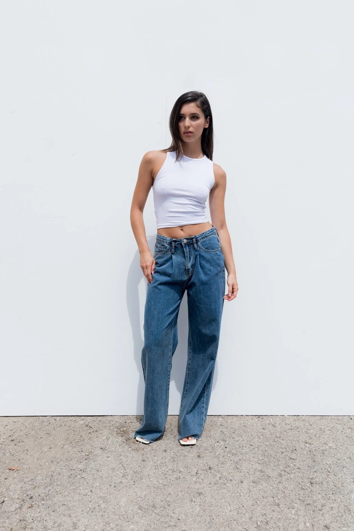 Femme portant un top blanc moulant sans manches en coton stretch et jeans bleus lâches