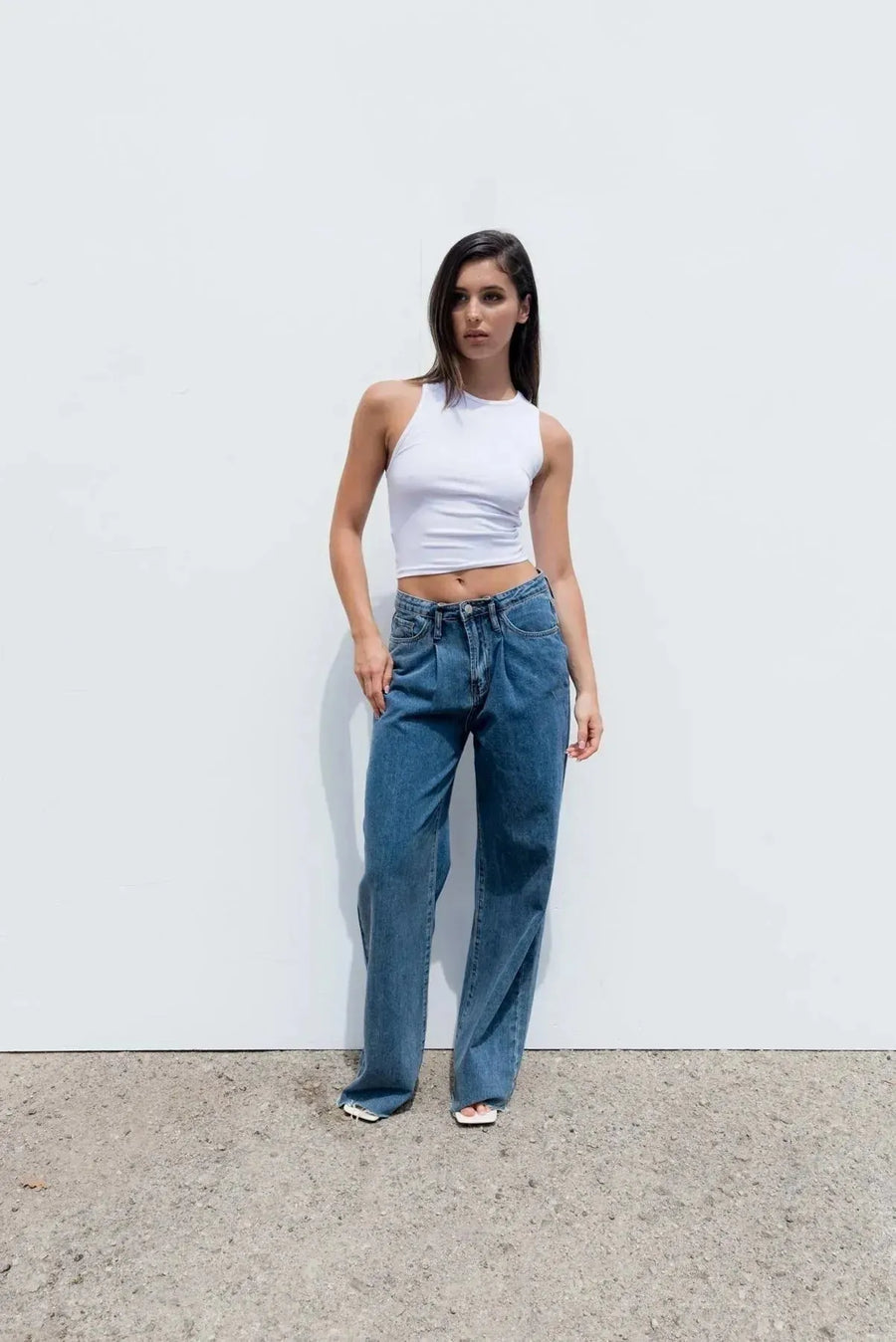 Femme portant un top blanc moulant sans manches en coton stretch et jeans bleus lâches