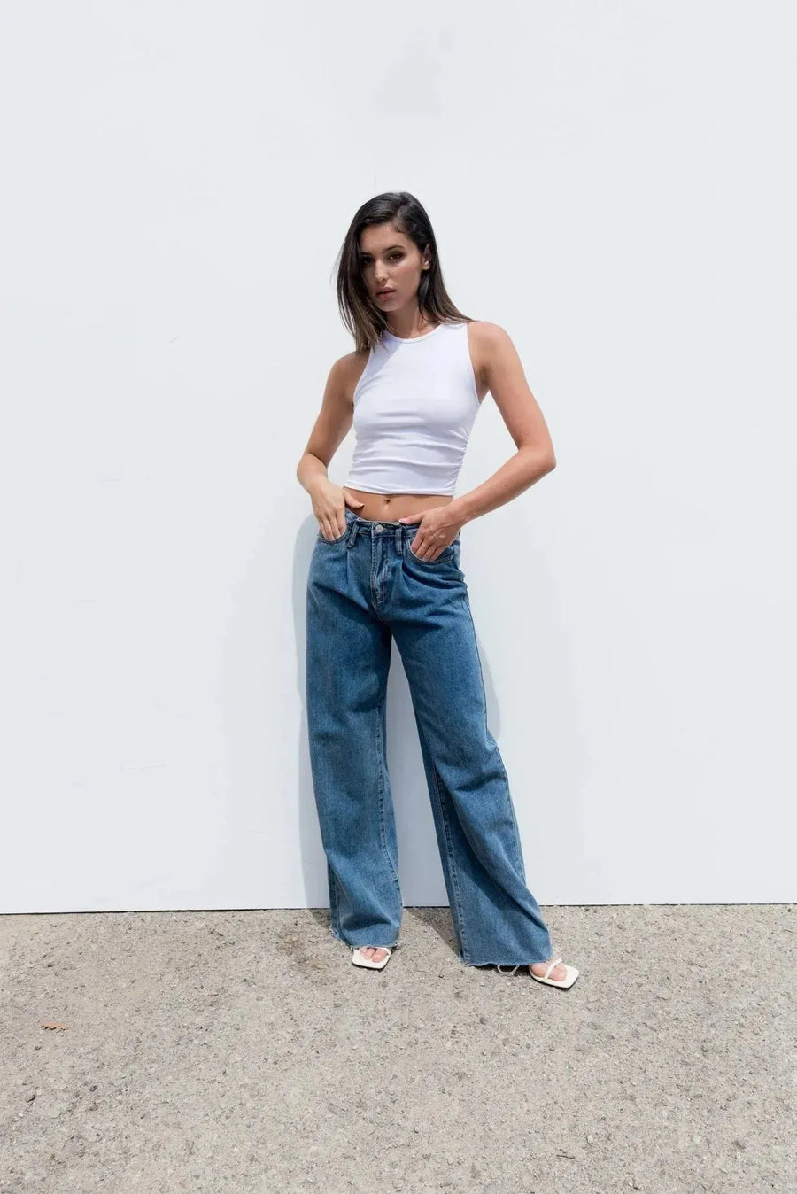 Femme portant un haut blanc moulant sans manches en coton stretch et jeans bleus