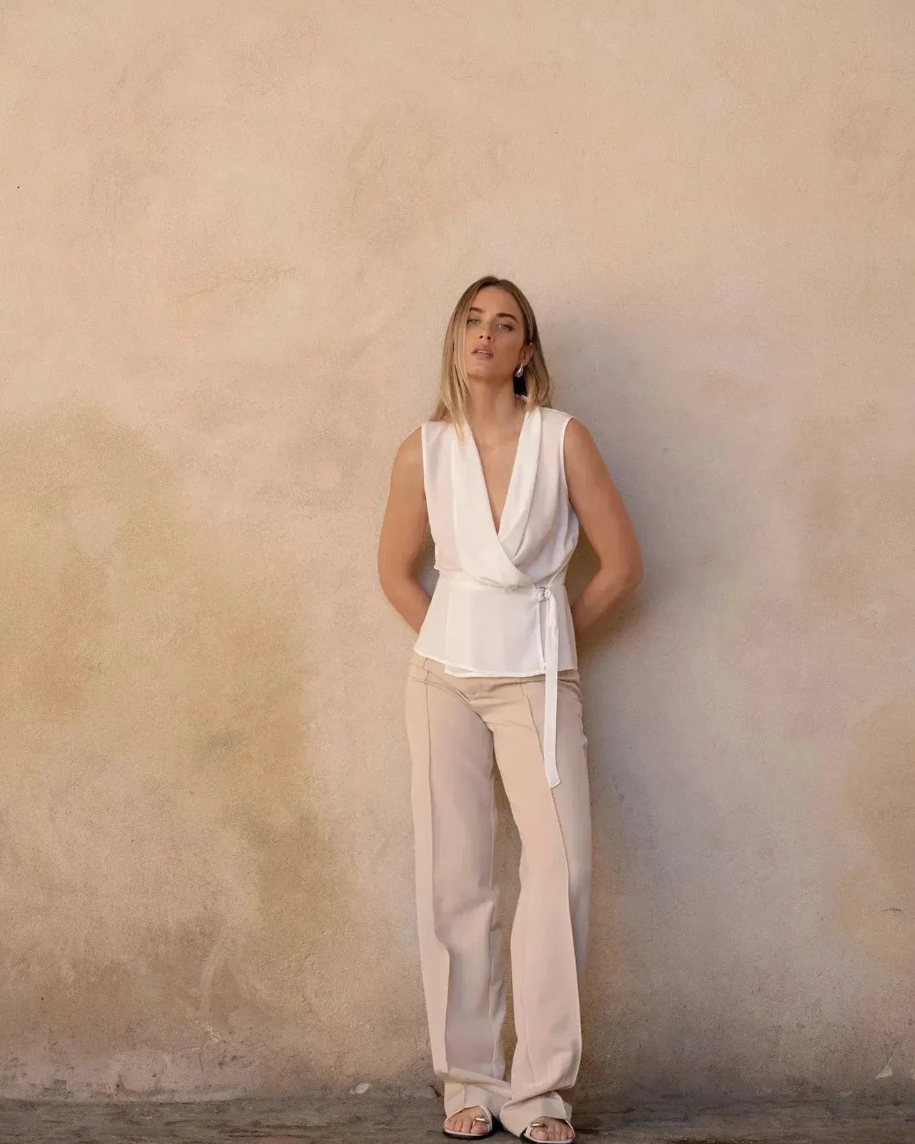 Femme élégante avec un haut blanc croisé sans manches, posant avec un pantalon cintré, un choix stylé de haut blanc femme.