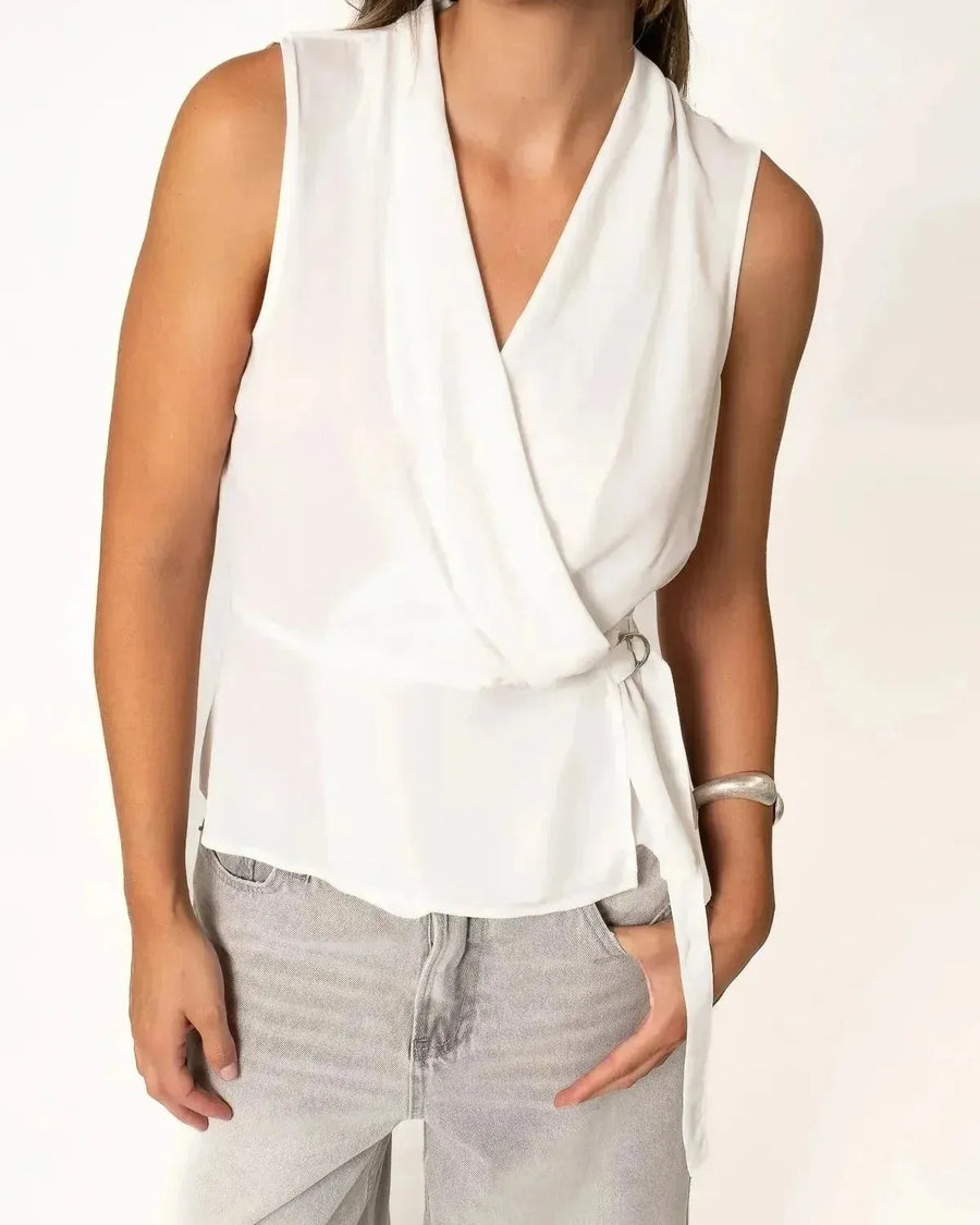 Femme portant un haut blanc croisé sans manches avec un jean, un look casual chic haut blanc femme.