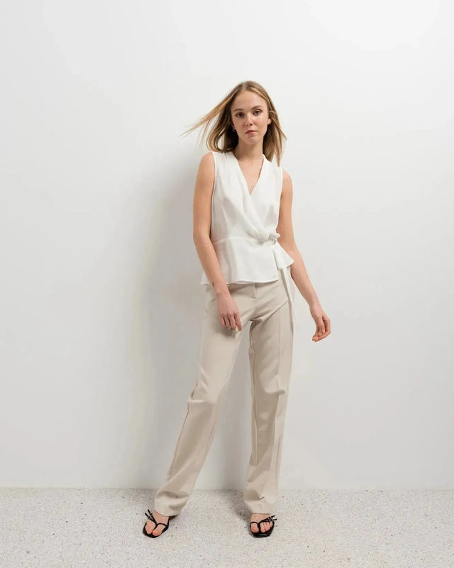 Femme souriante dans un haut blanc croisé sans manches et un pantalon beige, une tenue parfaite pour un haut blanc femme.