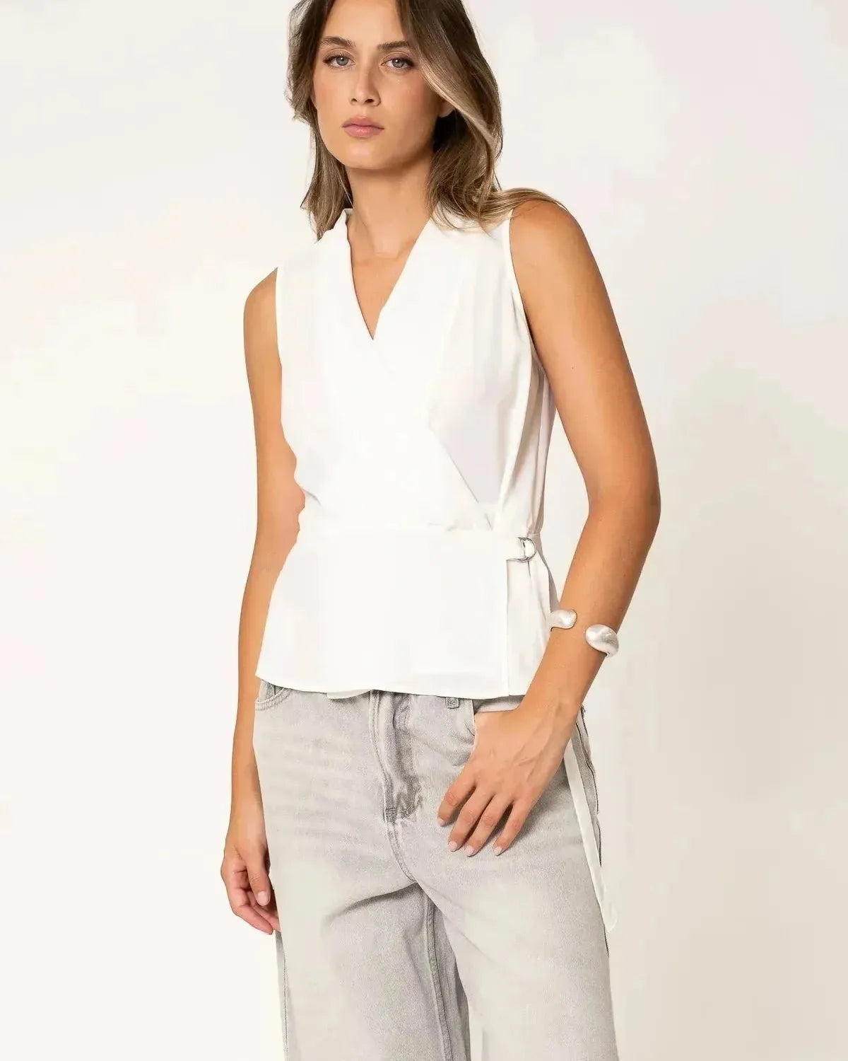 Modèle portant un top blanc croisé sans manches, un haut blanc femme élégant et décontracté.