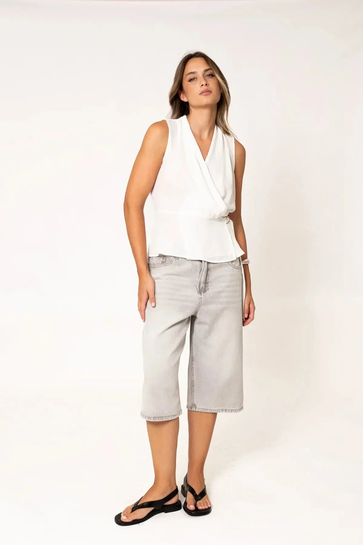 Top blanc croisé sans manches pour femme avec culottes en denim gris et sandales noires
