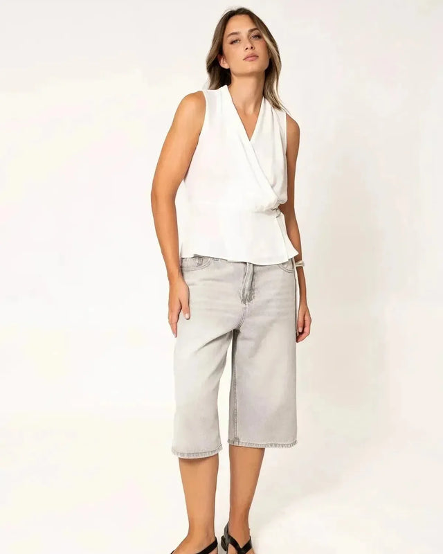 Modèle affichant un top blanc croisé sans manches, associé à un pantalon large, un essentiel dans les hauts blancs femme.