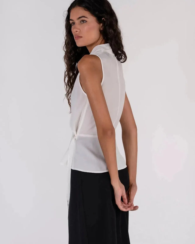 Femme de dos portant un haut blanc croisé sans manches, montrant le design échancré, un choix trendy pour un haut blanc femme.