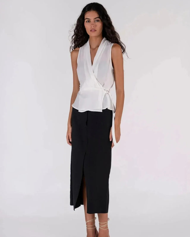 Femme posant dans un haut blanc croisé sans manches devant un mur beige, une tenue parfaite pour l’été avec ce haut blanc femme.