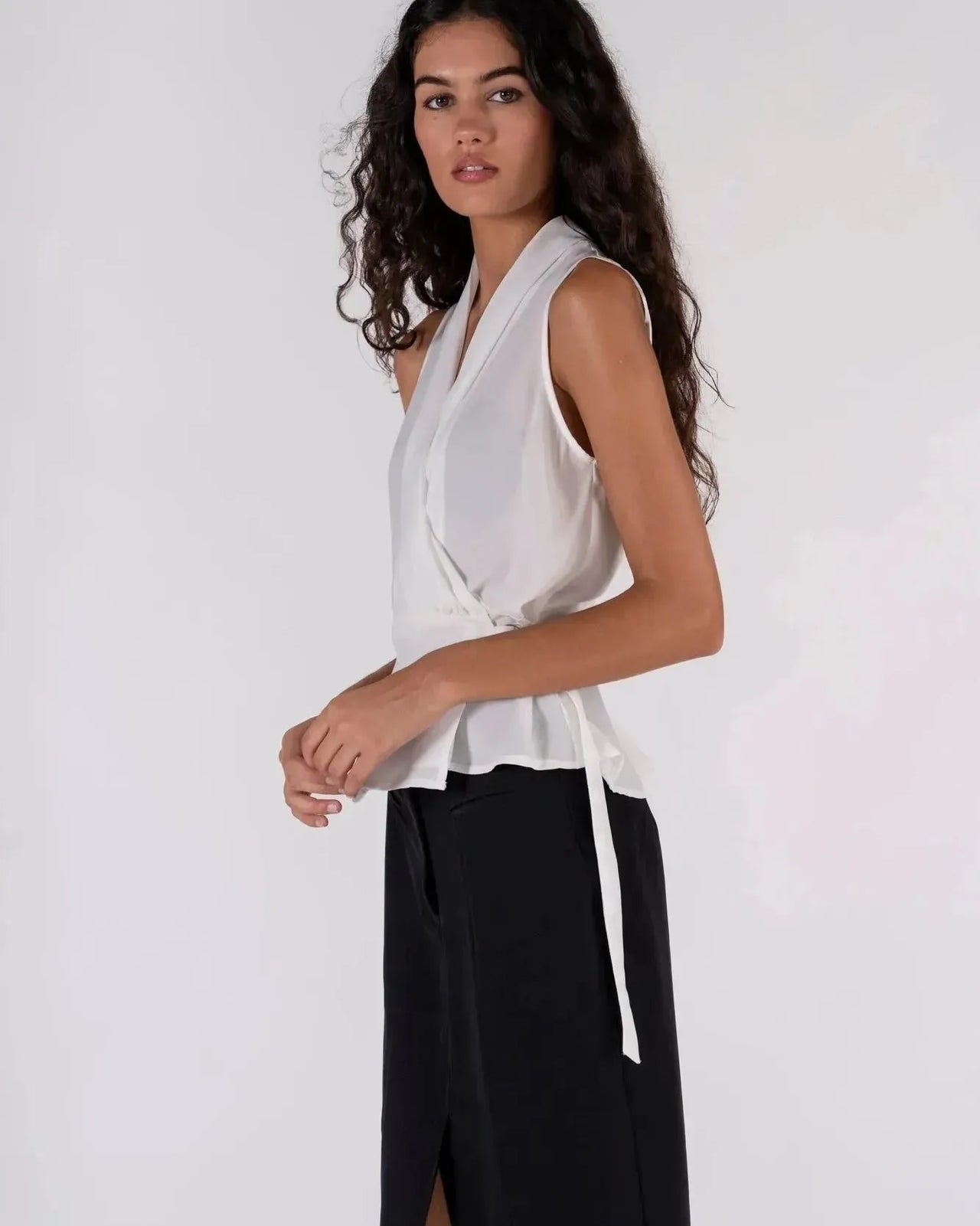 Femme avec un haut blanc croisé sans manches et un pantalon beige, un look simple mais chic avec ce haut blanc femme.