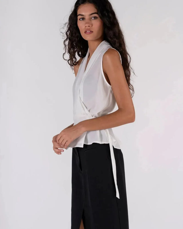 Femme avec un haut blanc croisé sans manches et un pantalon beige, un look simple mais chic avec ce haut blanc femme.